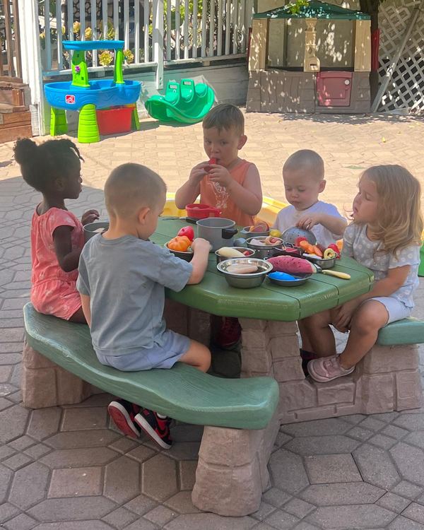 Children playing pretend kitchen at an outdoor picnic table