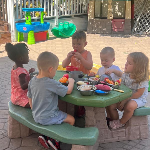 Children playing pretend kitchen at an outdoor picnic table