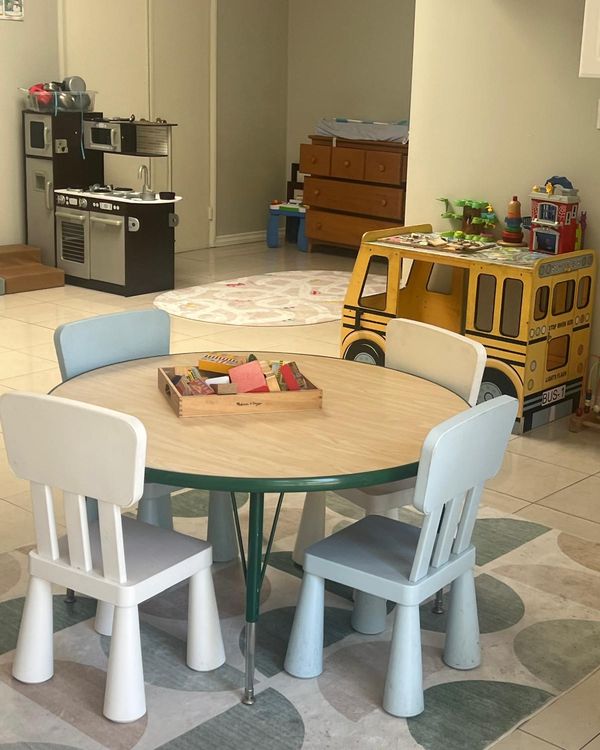 Bright indoor playroom with a round table, child-size chairs and a toy school bus